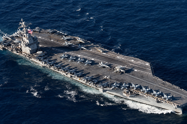 An aerial view of a gray US aircraft carrier sailing on deep blue water.